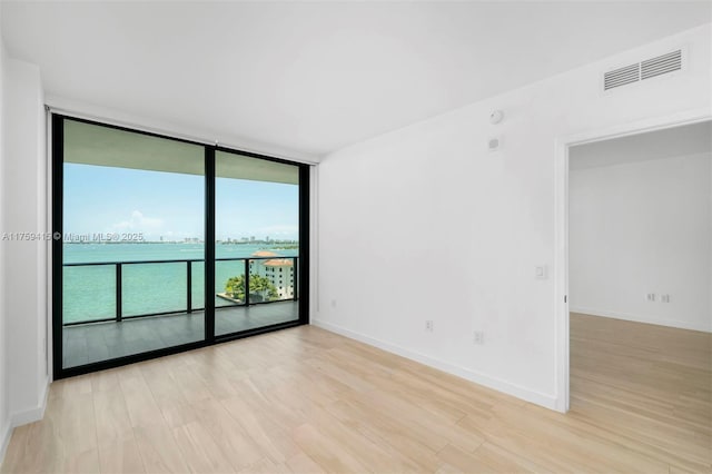 spare room featuring floor to ceiling windows, light wood-style floors, visible vents, and baseboards