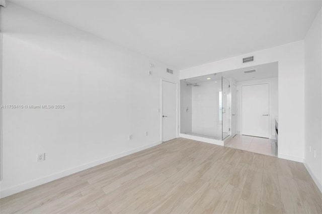 empty room featuring visible vents, light wood-type flooring, and baseboards