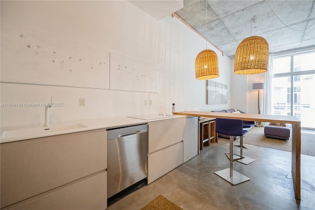 kitchen with concrete floors, a sink, light countertops, pendant lighting, and stainless steel dishwasher