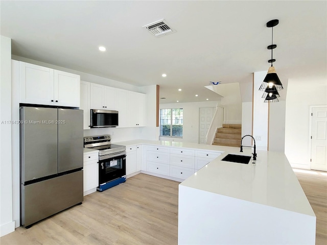 kitchen with visible vents, light wood finished floors, a sink, stainless steel appliances, and decorative light fixtures