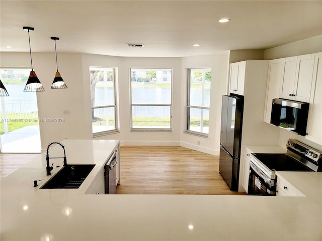 kitchen featuring pendant lighting, light countertops, light wood-style flooring, stainless steel appliances, and a sink