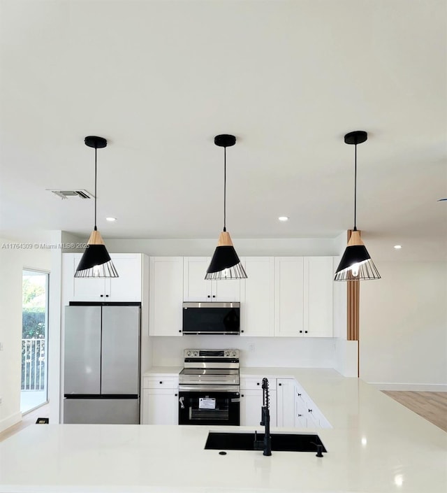 kitchen featuring a sink, stainless steel appliances, light countertops, pendant lighting, and white cabinetry