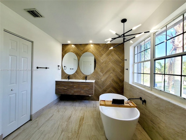 bathroom with visible vents, a freestanding bath, a closet, tile walls, and a notable chandelier