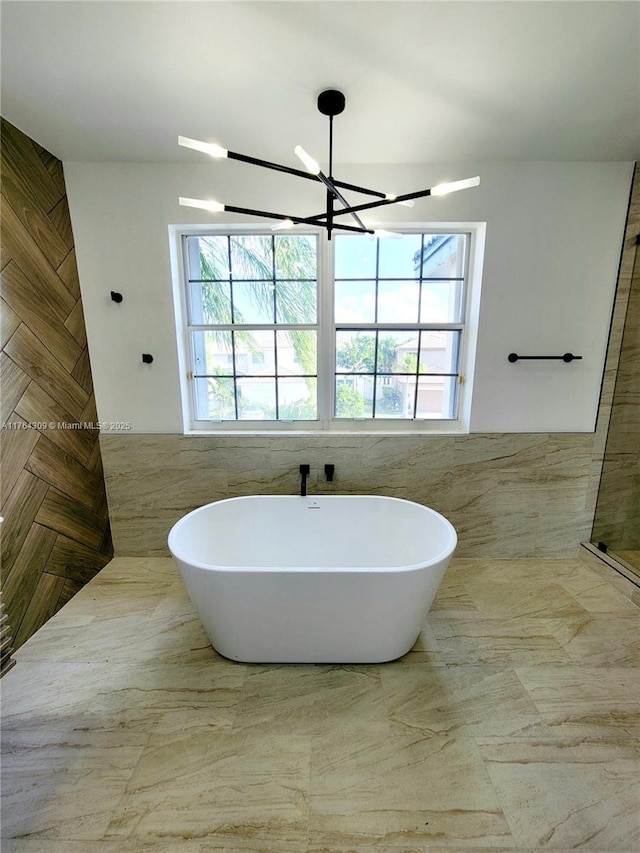 full bathroom featuring a notable chandelier, a freestanding bath, and tile walls