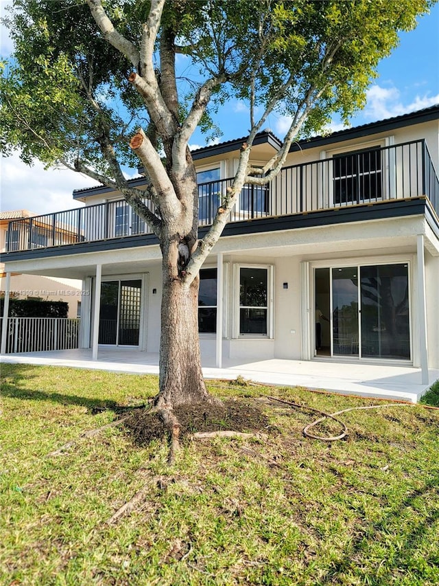 back of house with stucco siding, a patio, fence, a yard, and a balcony