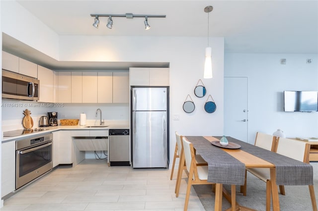 kitchen featuring modern cabinets, a sink, stainless steel appliances, light countertops, and hanging light fixtures