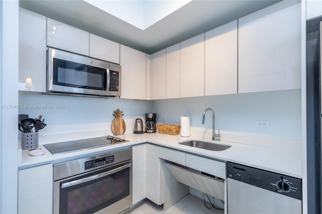 kitchen featuring white cabinets, stainless steel appliances, light countertops, and a sink