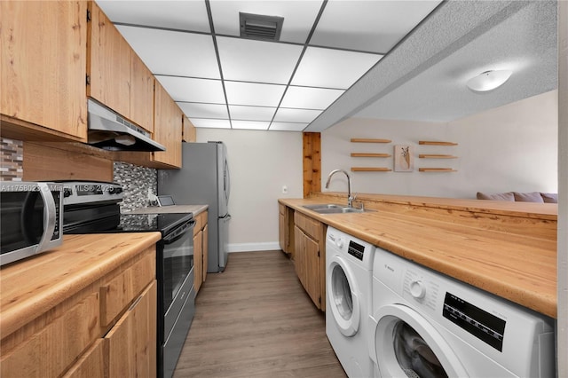 kitchen featuring a sink, black range with electric stovetop, under cabinet range hood, washer and dryer, and stainless steel microwave