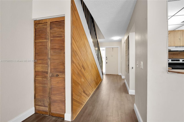 hall featuring stairway, a textured ceiling, baseboards, and wood finished floors