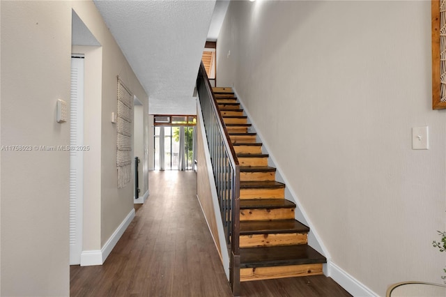 staircase featuring baseboards, a textured ceiling, and wood finished floors