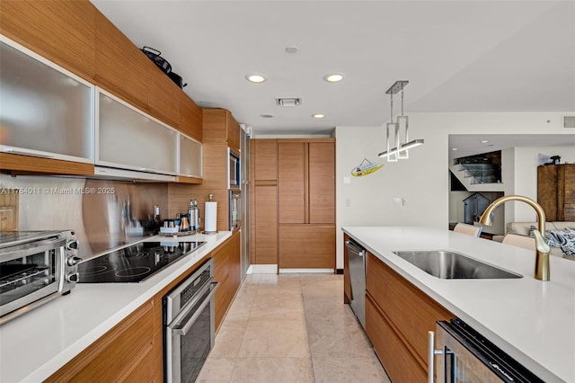 kitchen with modern cabinets, a sink, appliances with stainless steel finishes, brown cabinetry, and light countertops