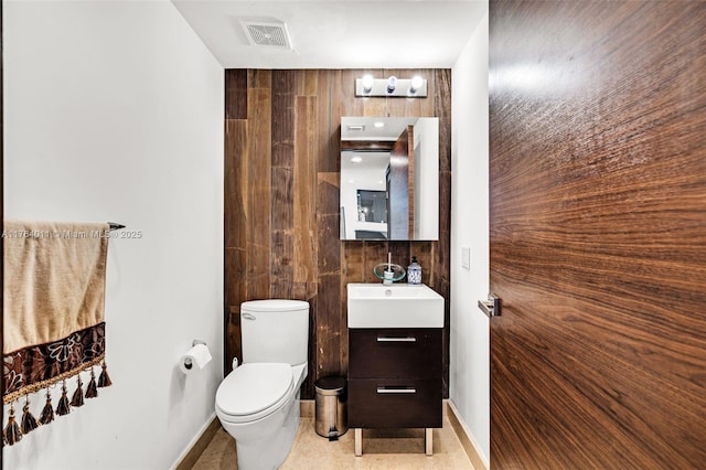 bathroom with vanity, wooden walls, baseboards, visible vents, and toilet