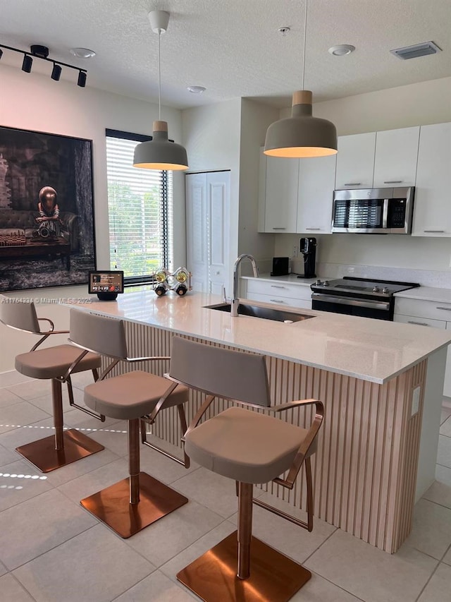 kitchen featuring an island with sink, electric stove, a sink, stainless steel microwave, and light stone counters