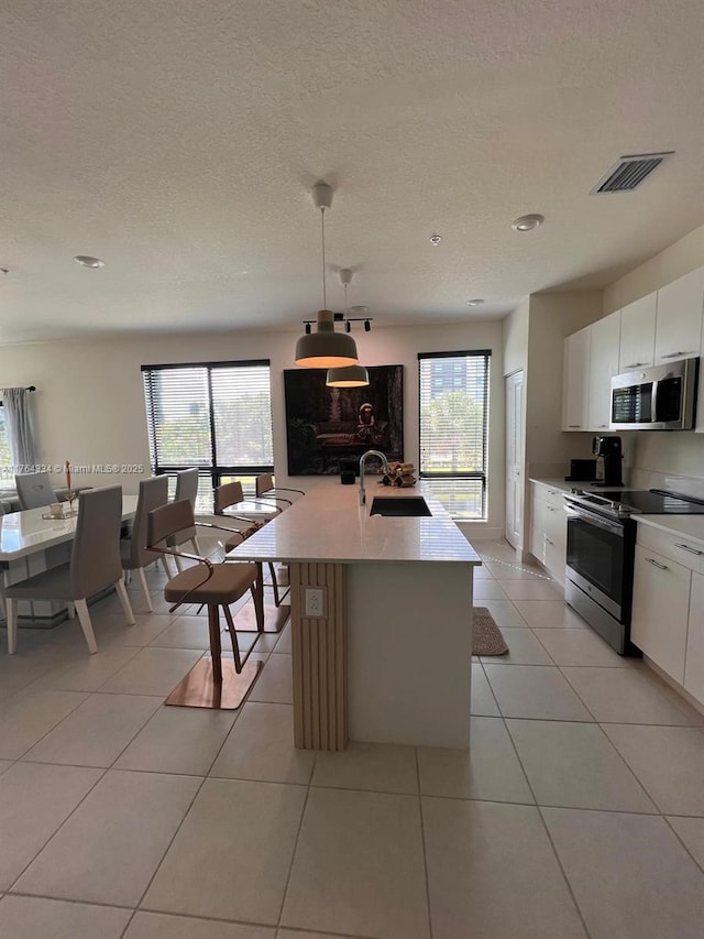 kitchen with a sink, pendant lighting, white cabinets, and stainless steel appliances