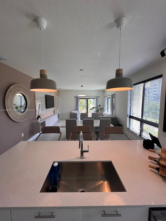 kitchen featuring a sink, light stone counters, a textured ceiling, open floor plan, and hanging light fixtures