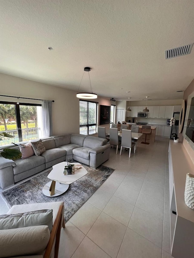 living room with light tile patterned floors, visible vents, a textured ceiling, and a wealth of natural light