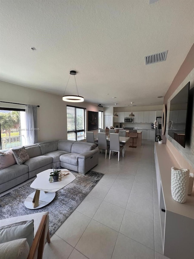 living room with light tile patterned floors, visible vents, a textured ceiling, and a wealth of natural light