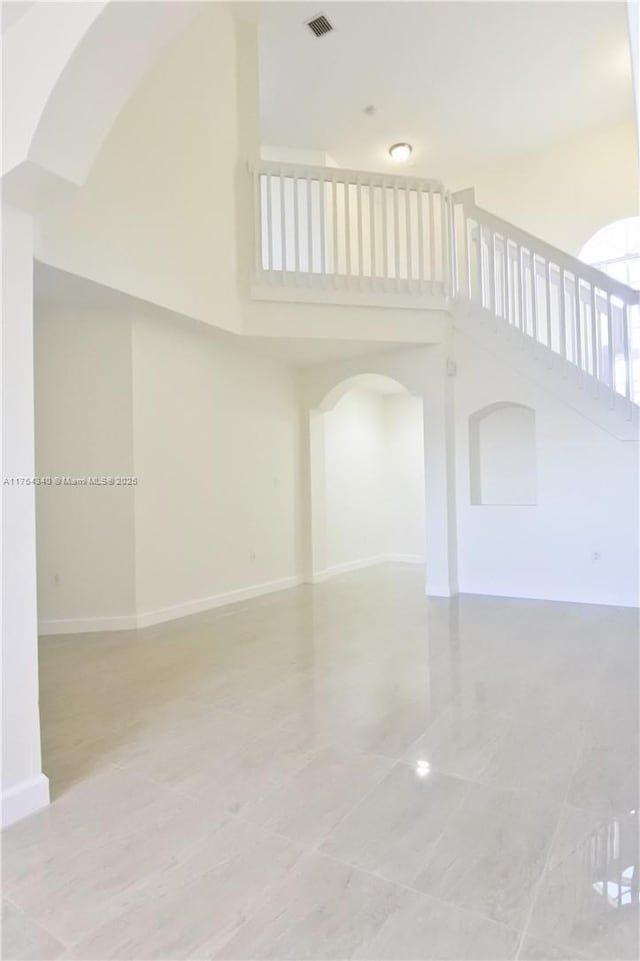 empty room featuring arched walkways, visible vents, baseboards, and a towering ceiling