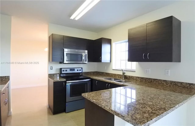 kitchen with dark stone counters, a peninsula, a sink, appliances with stainless steel finishes, and dark cabinets