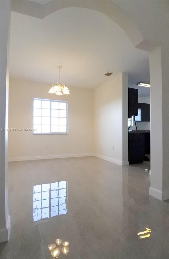 spare room featuring a chandelier, visible vents, arched walkways, and baseboards