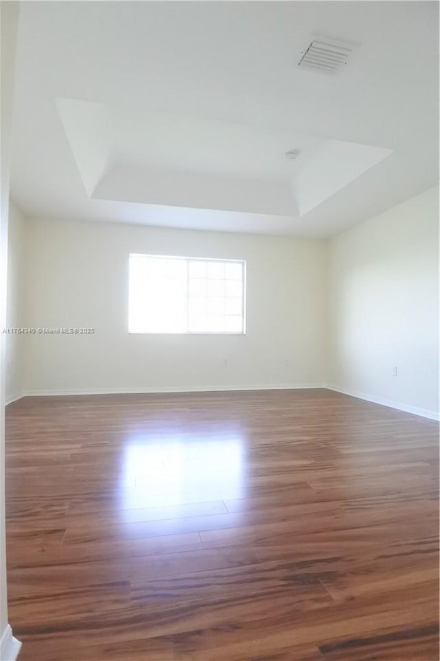 spare room with visible vents, a raised ceiling, and wood finished floors