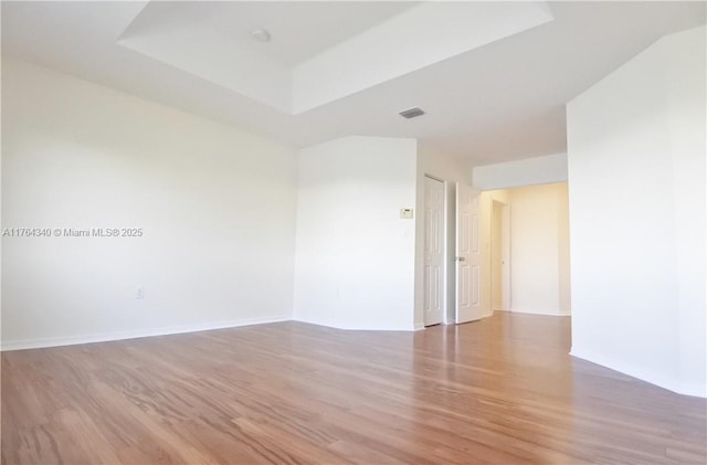 spare room with a raised ceiling, wood finished floors, visible vents, and baseboards