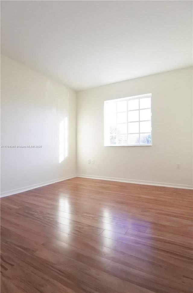 spare room with plenty of natural light, wood finished floors, and baseboards