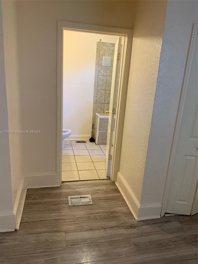 hallway with a textured wall, visible vents, baseboards, and wood finished floors