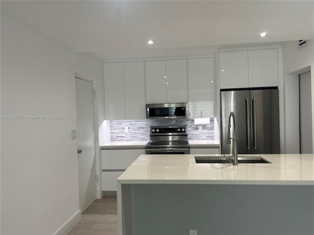 kitchen featuring modern cabinets, appliances with stainless steel finishes, light countertops, a sink, and backsplash