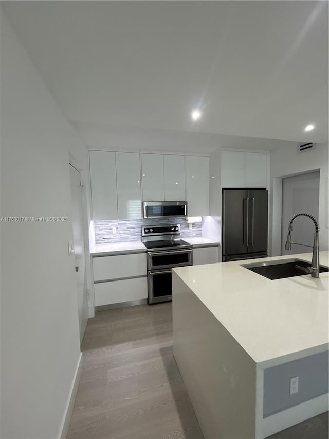 kitchen featuring modern cabinets, a sink, light wood finished floors, white cabinetry, and stainless steel appliances