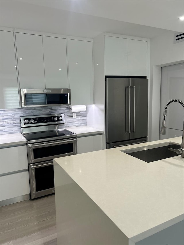 kitchen with tasteful backsplash, modern cabinets, appliances with stainless steel finishes, light wood finished floors, and a sink