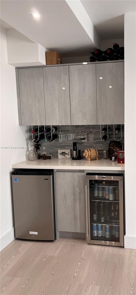 bar with bar, refrigerator, light wood-type flooring, and wine cooler