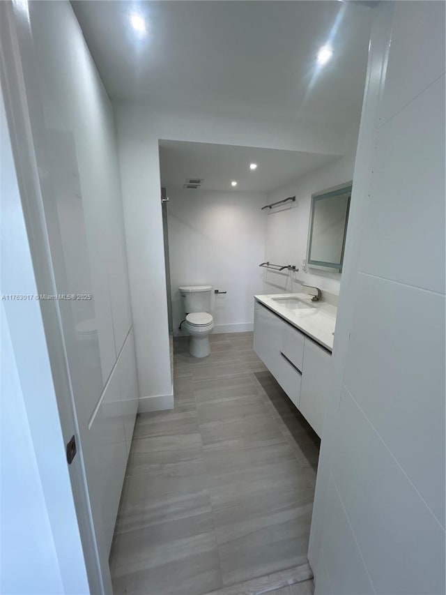 bathroom featuring visible vents, baseboards, toilet, recessed lighting, and vanity