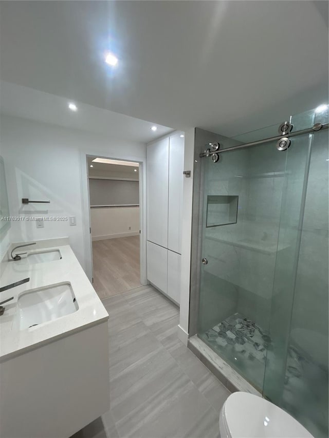 full bathroom featuring double vanity, a stall shower, recessed lighting, toilet, and a sink