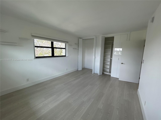 unfurnished bedroom featuring multiple closets, wood finished floors, and baseboards