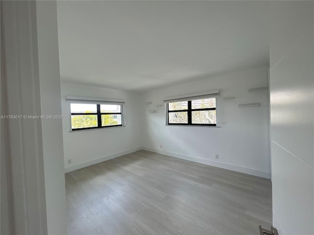 unfurnished room featuring a wealth of natural light, light wood-type flooring, and baseboards