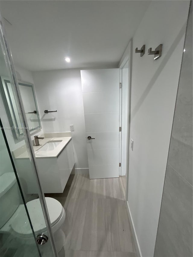 bathroom with toilet, wood finished floors, vanity, and baseboards