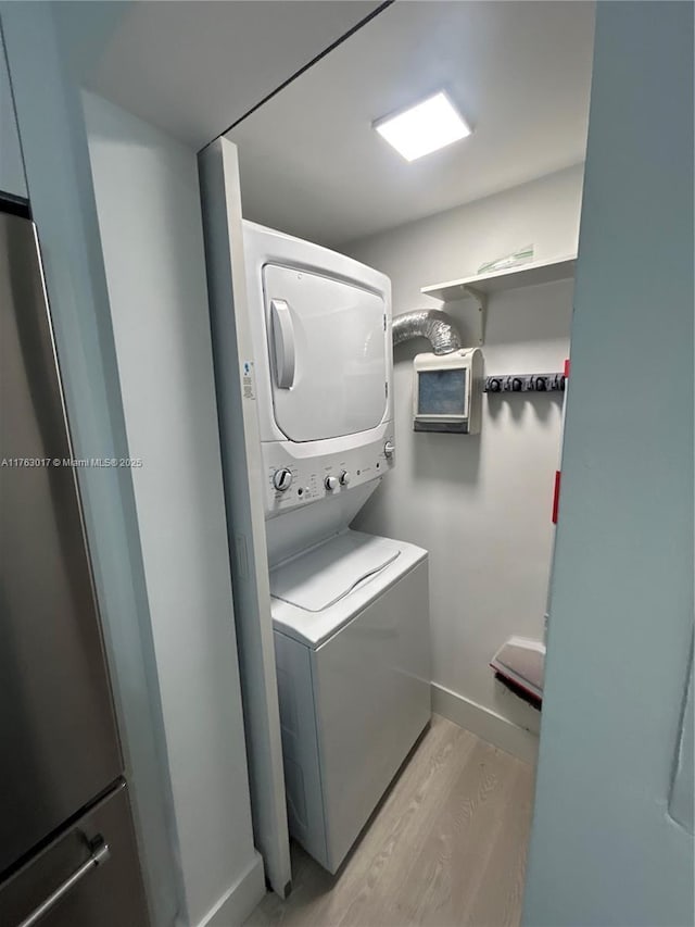 washroom with light wood-style flooring, laundry area, stacked washer and dryer, and baseboards