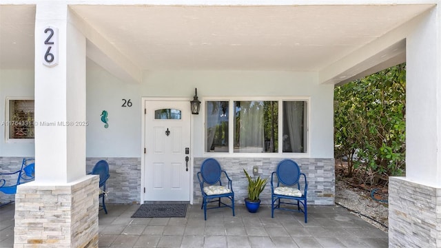 doorway to property featuring stone siding, stucco siding, and covered porch