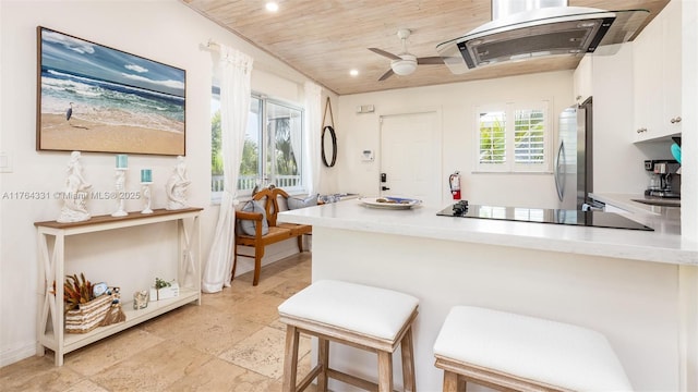 kitchen with a kitchen bar, freestanding refrigerator, a peninsula, white cabinets, and wooden ceiling