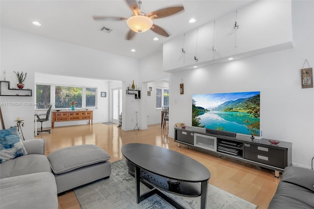 living area with visible vents, a ceiling fan, recessed lighting, light wood finished floors, and a towering ceiling