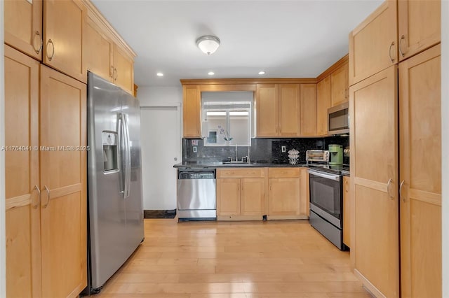 kitchen with light brown cabinets, appliances with stainless steel finishes, light wood-type flooring, and dark countertops