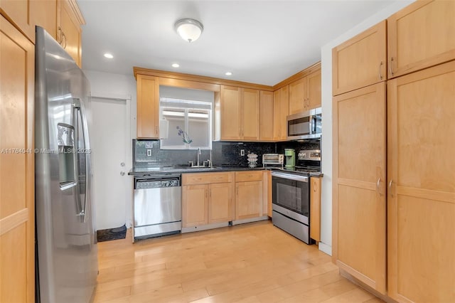 kitchen with light wood finished floors, dark countertops, light brown cabinets, appliances with stainless steel finishes, and a sink