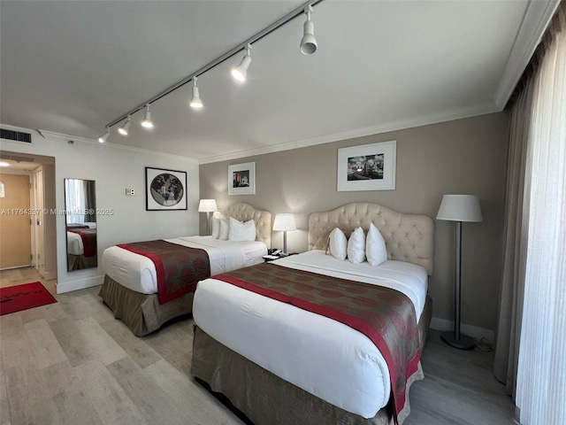 bedroom featuring light wood finished floors, visible vents, baseboards, and ornamental molding