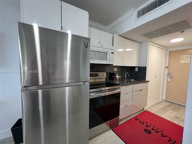 kitchen with visible vents, backsplash, stainless steel appliances, light wood-style floors, and white cabinetry