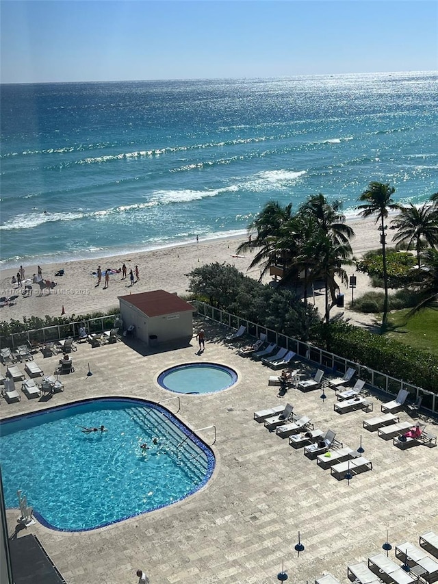 community pool featuring a water view, a community hot tub, fence, a view of the beach, and a patio area