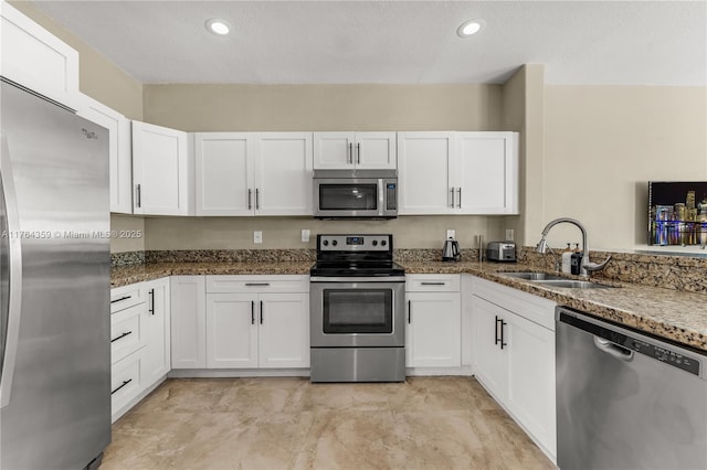 kitchen with a sink, dark stone counters, white cabinets, and stainless steel appliances