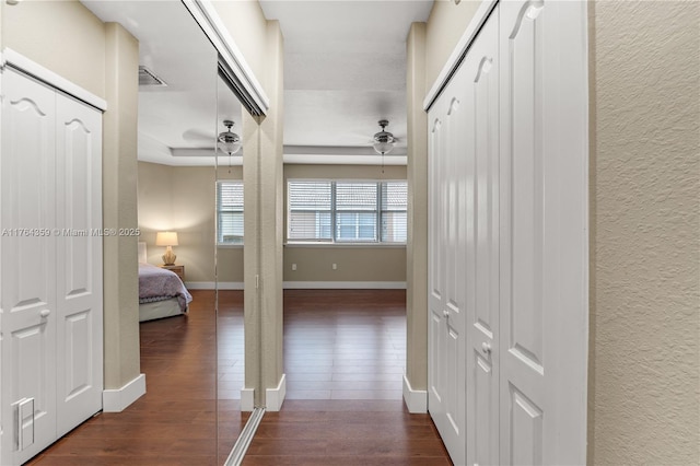 hallway with visible vents, baseboards, dark wood-style floors, and a textured wall