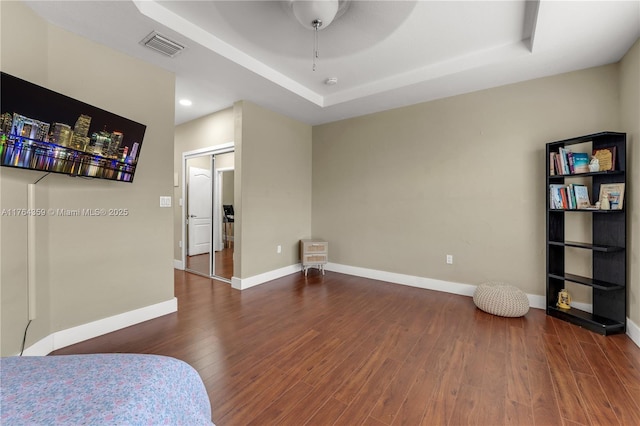 bedroom featuring visible vents, baseboards, a tray ceiling, and wood finished floors