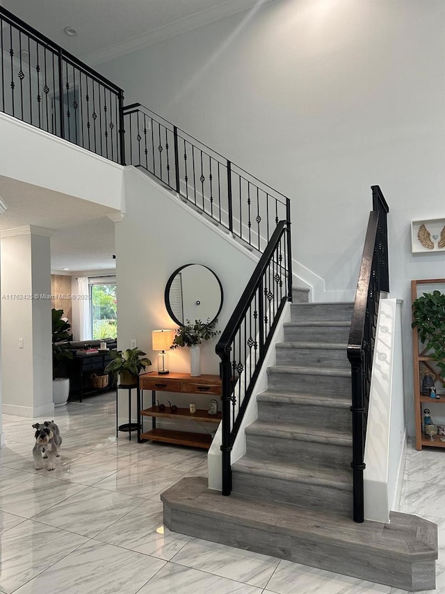 staircase featuring crown molding, baseboards, marble finish floor, and a towering ceiling